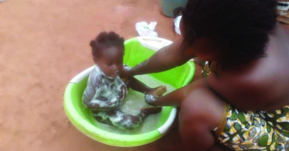 A mother cleaning her baby in a plastic tub.